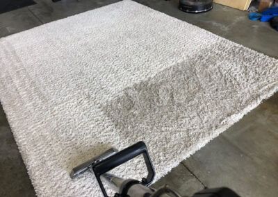 Почистване на голям бял килим с прахосмукачка.